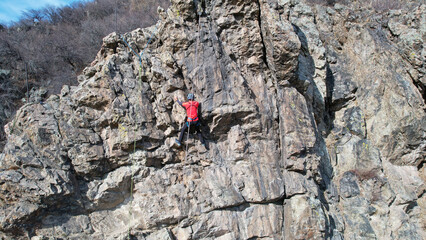 Rock climbing training on a steep slope in the mountains. The view from the drone. A group of people climb to the top of cliff. Brave girls and boys are looking for a trail on a cliff. Extreme sports