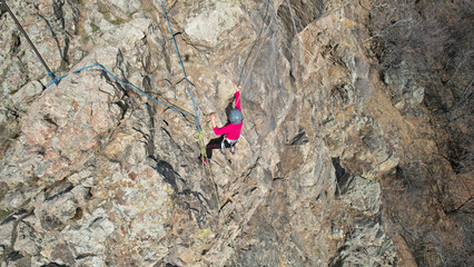 Rock climbing training on a steep slope in the mountains. The view from the drone. A group of people climb to the top of cliff. Brave girls and boys are looking for a trail on a cliff. Extreme sports