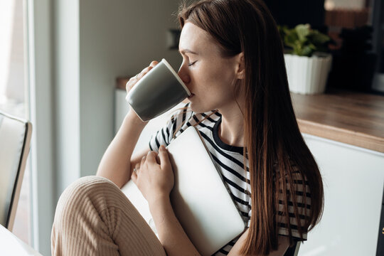 Portrait of beautiful young woman drinking and taking sips of morning refreshing coffee in light modern kitchen closeup side view. Lady with closed eyes enjoying taste of drink, waking up