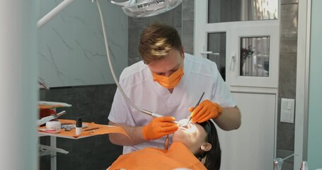 dental hygiene, dentist man in mask and sterile gloves doing teeth cleaning for patient who with dilator in mouth lies in chair in dental clinic