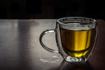 Fresh tea from rose petals in glass cup. Pink hot drink on dark brown background