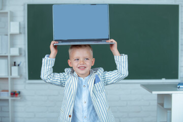 Fototapeta na wymiar Kid boy holding laptop on head, learning lesson at school, using gadget.