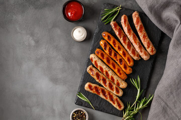 Assorted grilled sausages on barbecue with sauces. Assortment of different sausages on slate board and dark background.