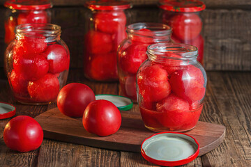 canning of red ripe tomatoes in their own juice, on a wooden background there are glass jars in...