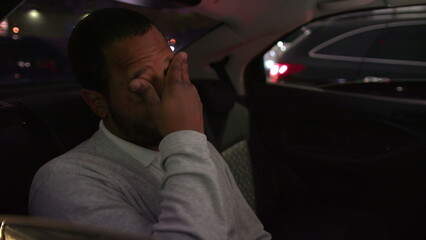Anxious person in car backseat commuting at night after work inside taxi cab. Worried emotion of one black man inside car
