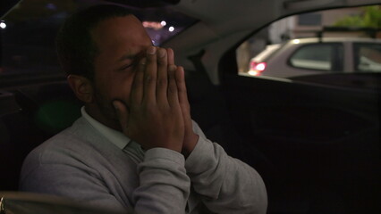 Anxious person in car backseat commuting at night after work inside taxi cab. Worried emotion of one black man inside car