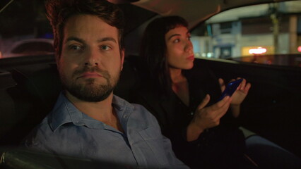 Pensive man in car backseat stuck in traffic at night after with with female partner looking at smartphone device waiting for vehicle to move