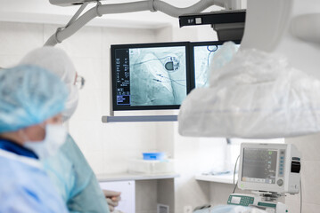 a cardiac surgeon in the operating room, observes on x-ray monitors, a pacemaker installed in a...