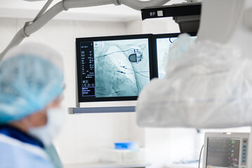 the surgeon observes on x-ray monitors, an implanted pacemaker connected to the heart....