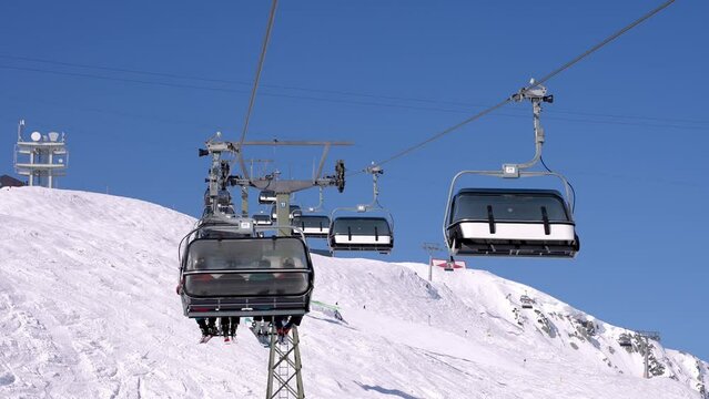 Ski lift moving over snowy landscape in Austrian Alps. Chairlift against clear blue sky. Tourists enjoying winter in the ski resort in Alps.
