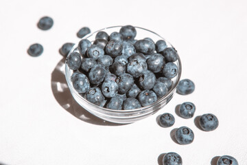 Blue blueberry in bowl and heap of berries on white table, card with organic sweet food