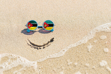 A painted smile on the sand and sunglasses with the flag of Mozambique. The concept of a positive...