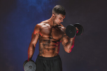 Plakat Brutal sweaty strong young man athlete with naked upper body standing doing workout with dumbbels and showing strong pumped up biceps over smoky background. Sport men body concept