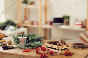 Focus on wooden table with Christmas decorations and hand tools used for making wreath in modern workshop