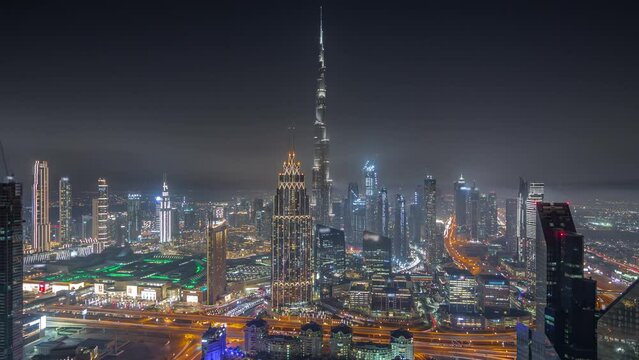 Aerial panoramic view of tallest towers in Dubai Downtown skyline and highway night timelapse. Financial district and business area in smart urban city. Skyscraper and high-rise buildings