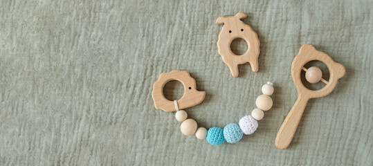 Wooden baby toys on green canvas background. Trendy eucalyptus color. Flat lay, copy space, top view. Sustainable early childhood development. Eco accessories, rattle and teethers for newborn
