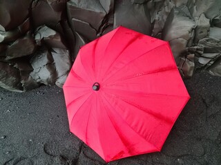 A lone red umbrella on the endless black beaches of Iceland in front of black basalt rock...