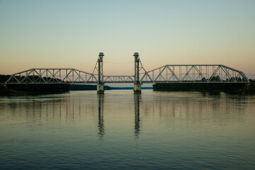 Modern metal bridge for transport across the river. The bridge is located outside the city, against the backdrop of sunset