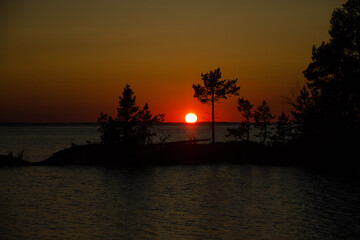 Sunset on Lake Ladoga on a summer evening. The sun is setting below the horizon, the sky is orange.