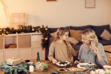 Happy excited young mother and braided daughter making beautiful holiday wreath while preparing home for Christmas
