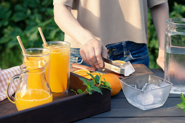 Girl cooking summer orange cocktail with mint and ice cubes outdoors, selective focus