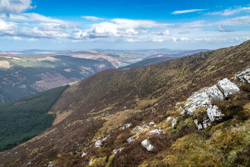 Fototapeta na wymiar View of Glenmalure valley during sunny day. It is U-shaped glacial valley in the Wicklow Mountains in Ireland. Base for accessing the mountain of Lugnaquilla. Saturated colors and dramatic sky.