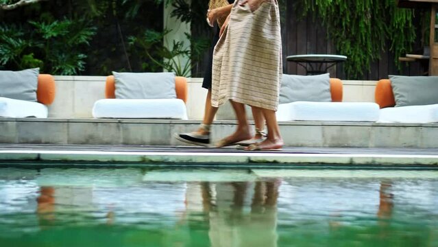 Legs of European ladies walking in long backyard dresses along the pool