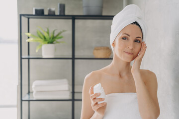 Face moisturizer, lifting cream. European lady applies face lotion or cream from bottle.