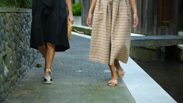 The European ladies walking in white long dresses down a narrow street with a small river