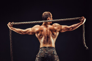 Back view of handsome sexual strong young man, muscular body holding rope with hands standing...