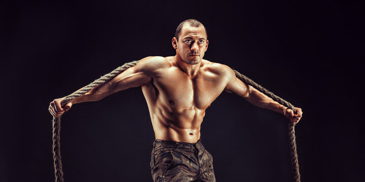 One handsome sexual strong young man, muscular body holding rope with hands hanging on neck and shoulders standing posing in studio on black background