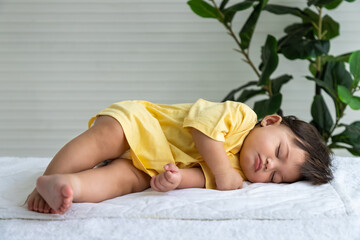 Little Asian baby girl lying down sleeping on bed at home. Newborn child relaxing in bed. Nursery for young children.