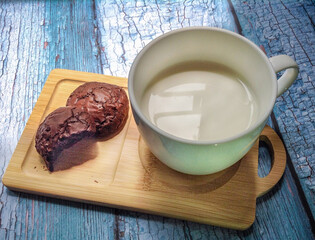 A glass of milk sits on a table with fresh bread and chocolate chip cookies nearby  for a breakfast or snack