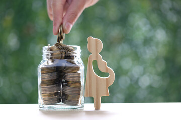 Pregnant woman with stack of coins money in glass bottle on natural green background,Save money for...