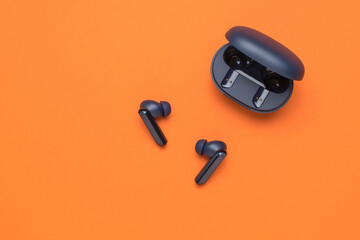 Blue wireless headphones with an open case on an orange background. A popular wireless gadget.