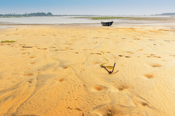 Moody image of a boat on water tied by a rope with an anchor on river bed. Tajpur, West Bengal, India. Minimalistic image.