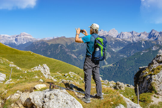 Active senior man hiking and taking pictures in Dolomiti mountains with backpack, enjoying his adventure. Carezza, Dolomites Alps, South Tyrol, Italy, Europe.