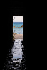 Afternoon view through an opening of an underpass of the rocks and beach around Petra tou Romiou,...