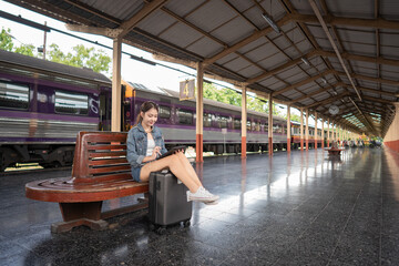 Fototapeta premium Asian young woman traveler sitting in a train station and using a digital tablet. Travel concept.