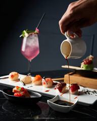 Close-up hand serving soy sauce. Detail of sushi set on wooden tray at restaurant. Japanese cuisine concept.