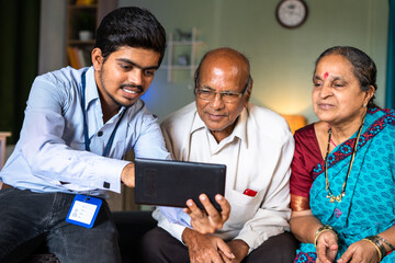 Banker showing insurance or financial replated plans on digital tablet to senior couple at home -...
