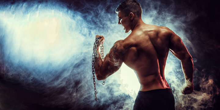 Handsome power athletic man bodybuilder doing exercises with chain. Fitness muscular body on dark background. Perfect male. 