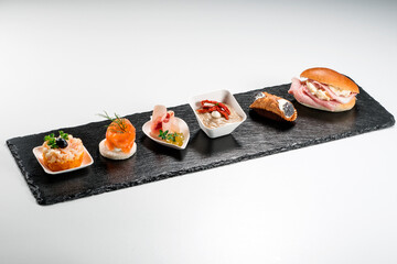 Black stone rectangular tray with shrimp tartare snack cannoli swordfish ravioli with robbiola tartina nordica mousse aubergine