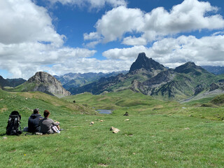 Fototapeta premium family of two people and a child rest sitting on the grass contemplating the landscape around the peak of the Midi d'Ossau in the French Pyrenees