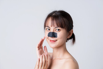 Beautiful Asian female model applying mask charcoal deep cleansing nose pore strip on fresh clean skin.