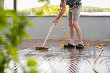 Body of a man with a scrubbing brush and a water hose making spring cleaning on a wooden terrace