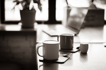 Coffee cups and laptop on table, sepia toned. Coffee break. Idyllic place for work. Freelance work place. Morning with coffee and notebook. Cafe interior. Creative space for work. Hot morning drinks.