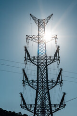 High voltage electrical towers, backlit, with blue sky on a sunny day.