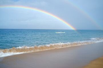 A rainbow arcs above a canoe in the ocean off Maui, Hawaii