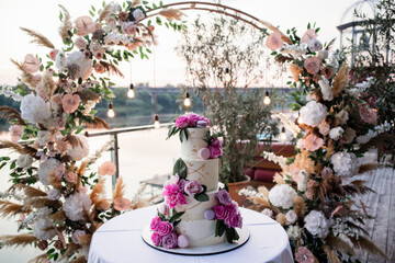 large beautiful wedding cake in the evening near the arch with decor